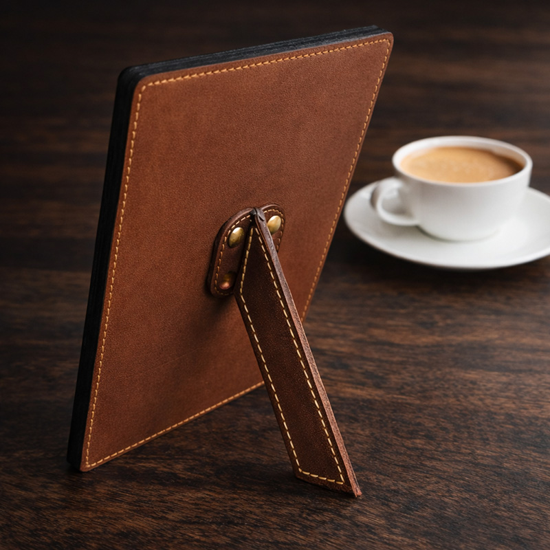 The back of a genuine leather frame with brass support stand, placed next to a coffee cup on a wooden table