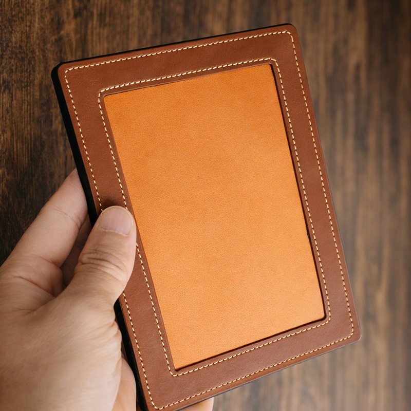 Hand holding a genuine leather frame showing the front with double-stitched border and inner panel